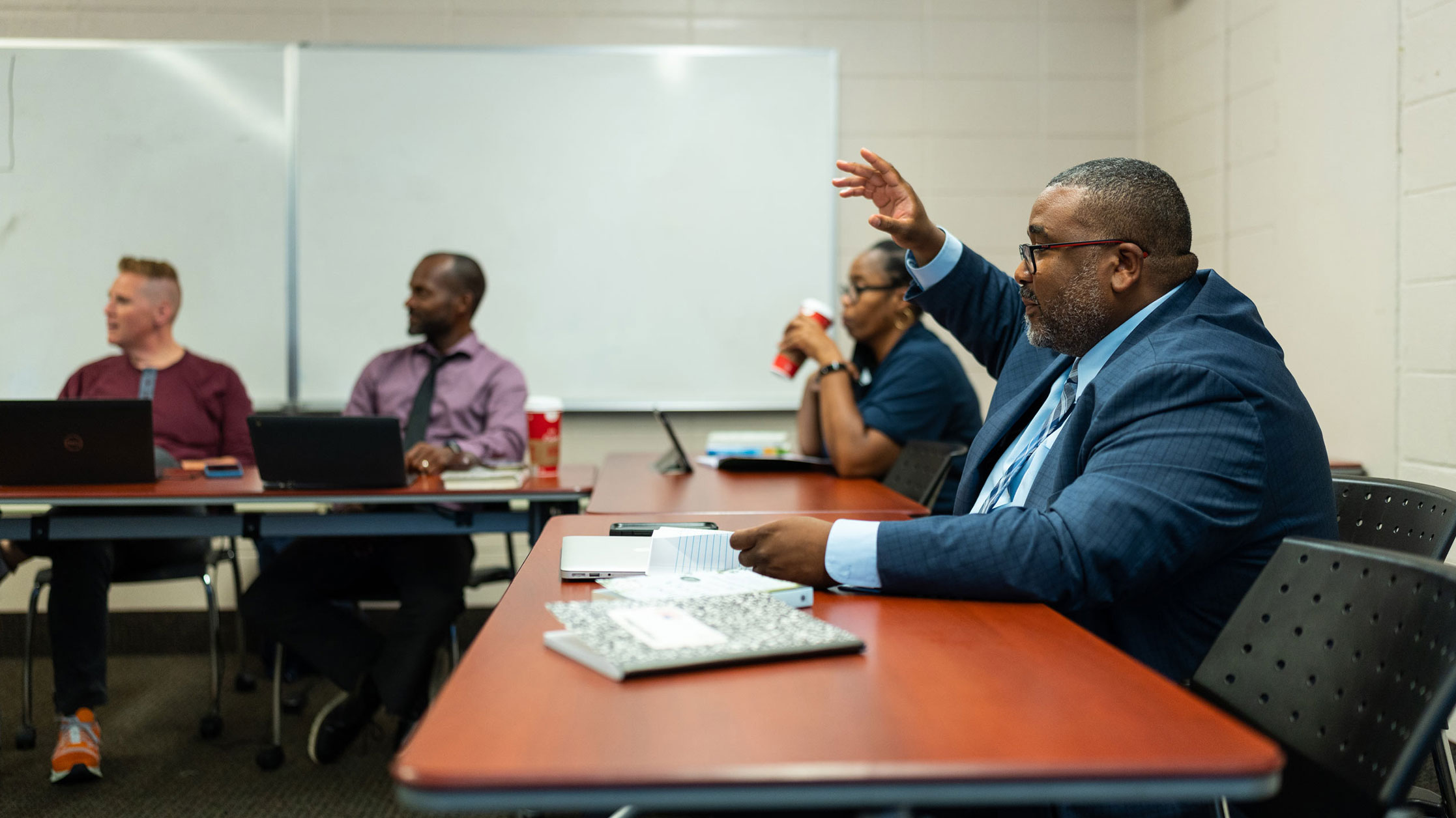 Education leadership classroom with student in blue suit raising his hand