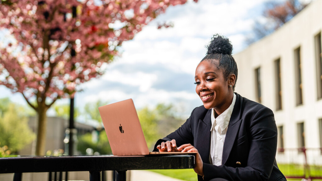 Educational Leadership student sitting at picnic table with open laptop