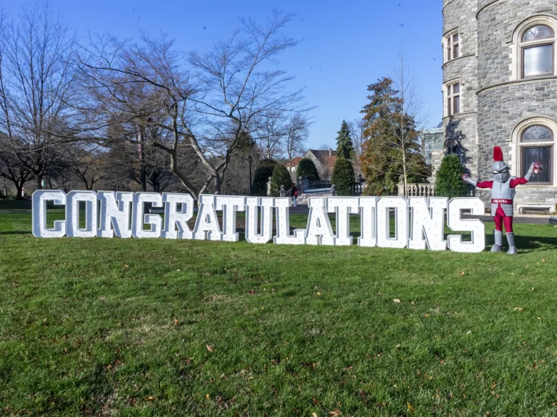 Arcadia's mascot, Archie stands by a 3D sign that says congratulations.