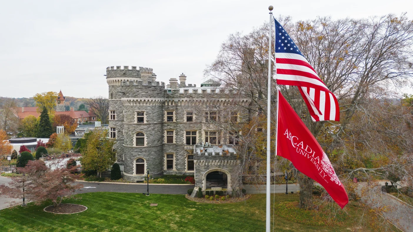 An American and Arcadia flag fly in front of Grey Towers Castle on a cloudy fall day.