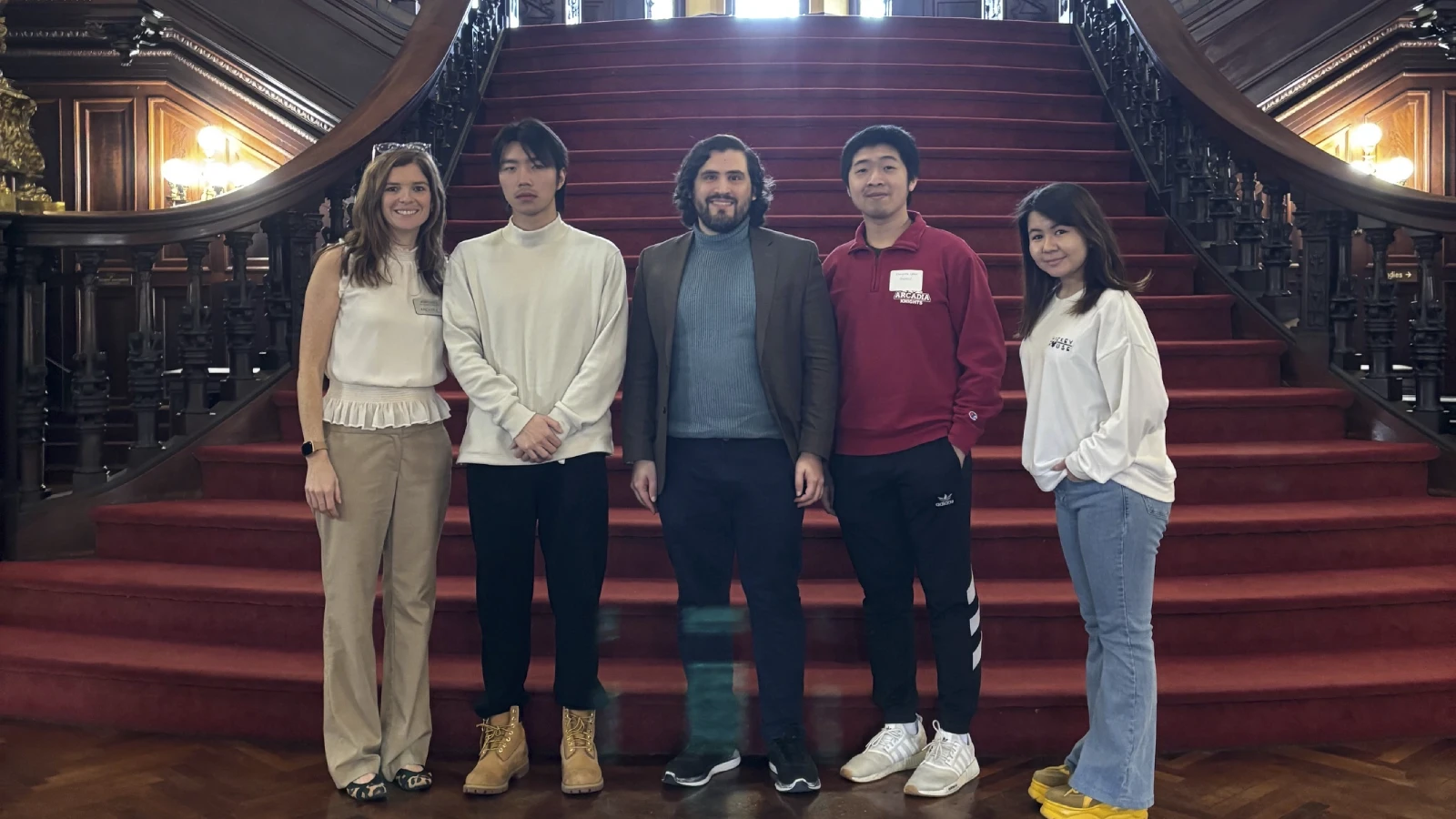 Four international students and an admissions staff member stand on the red carpeted steps inside Grey Towers Castle.