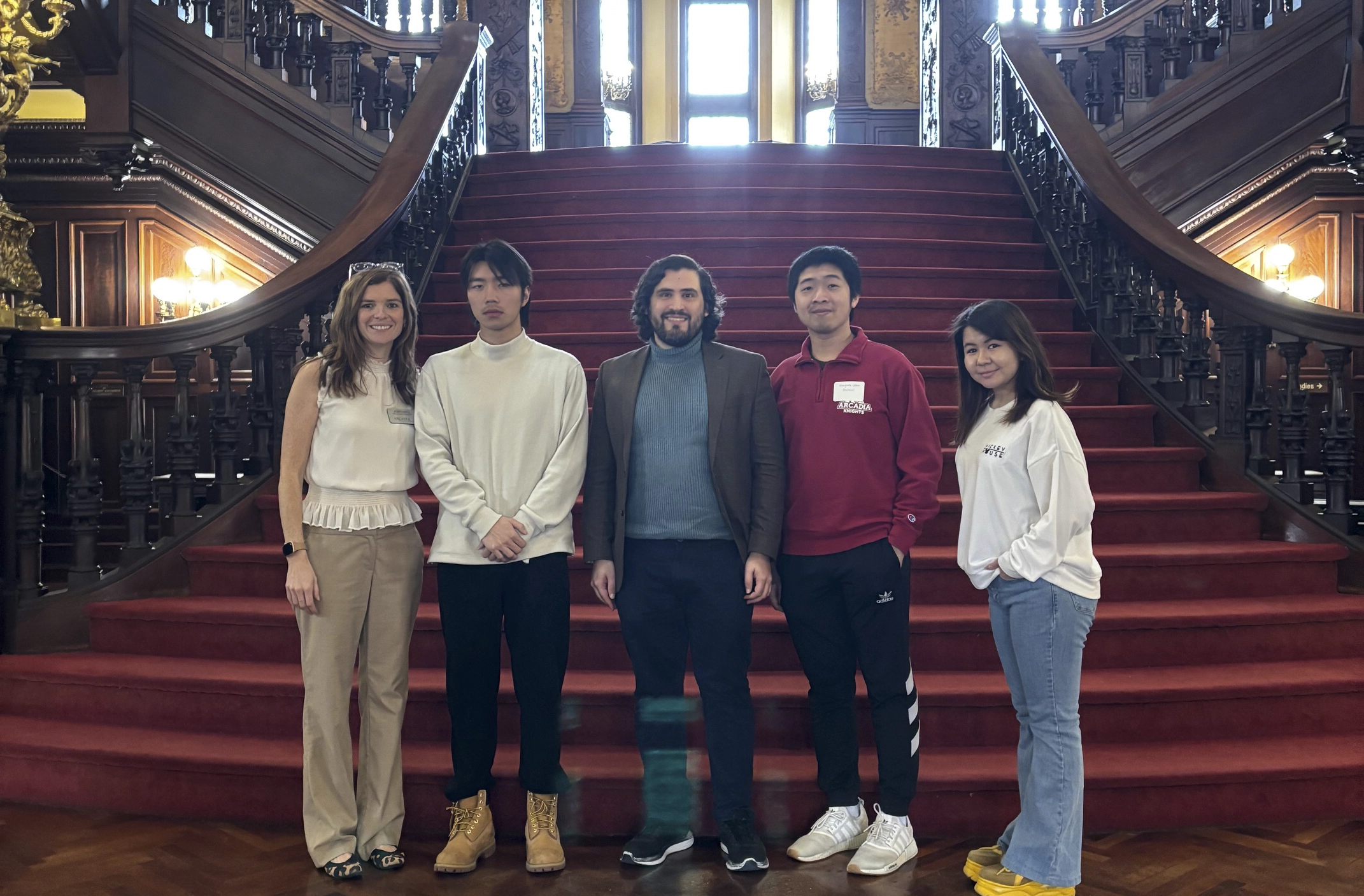 Four international students and an admissions staff member stand on the red carpeted steps inside Grey Towers Castle.