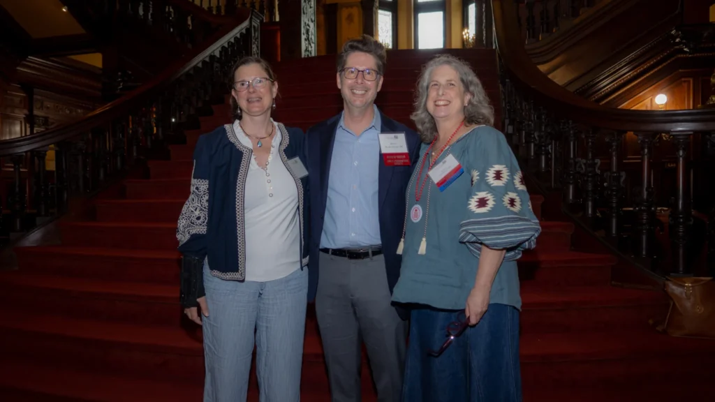 Three alumni standing and smiling in front of the Grey Towers Castle staircase.
