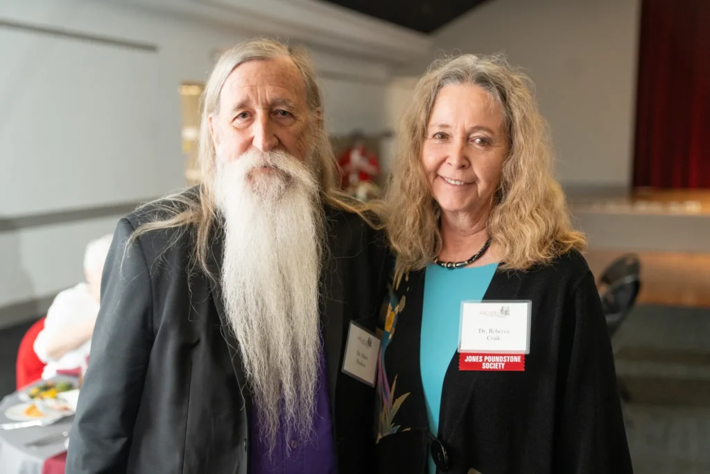 A woman and a man with a long white beard stand smiling together.