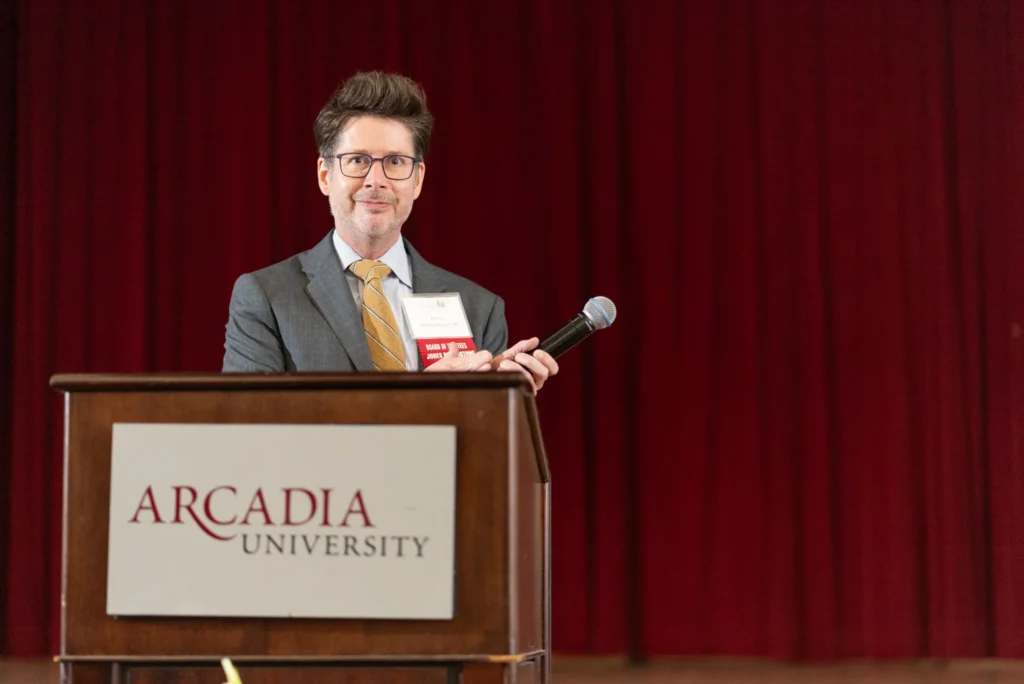 Man standing at the podium with microphone in his hand and clapping.