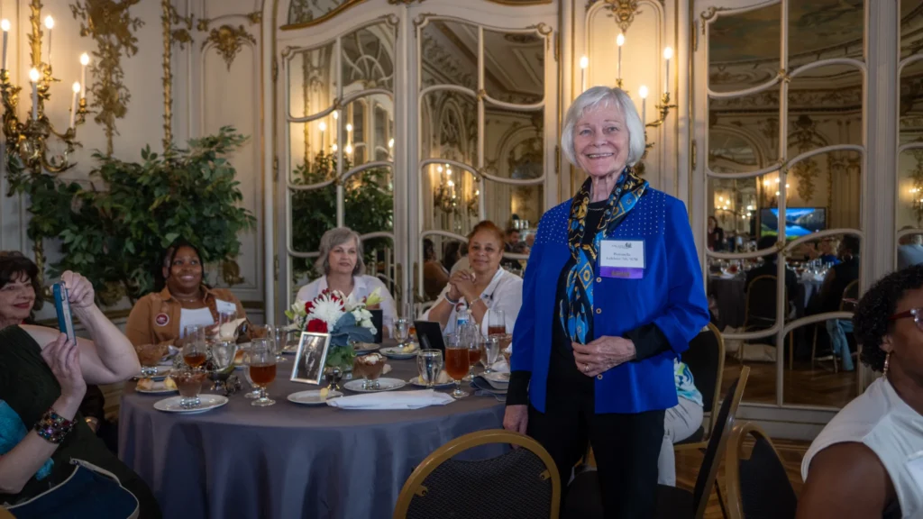 Woman with white hair standing up at her table to accept her recognition.