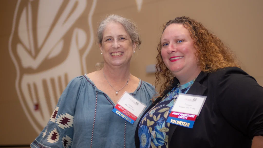 Two women posed and smiling wearing Jones Poundstone Society Volunteer badges.