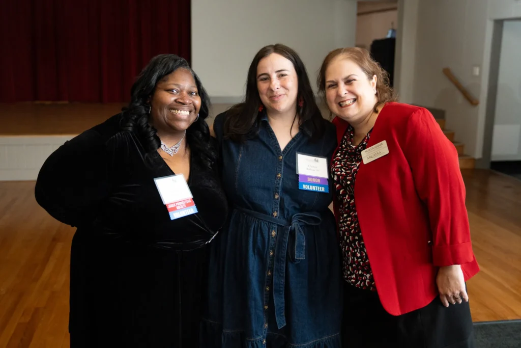 Three women standing together with the arms around each other smiling.