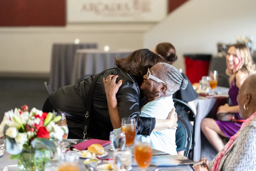 Two women are hugging around a circle table.