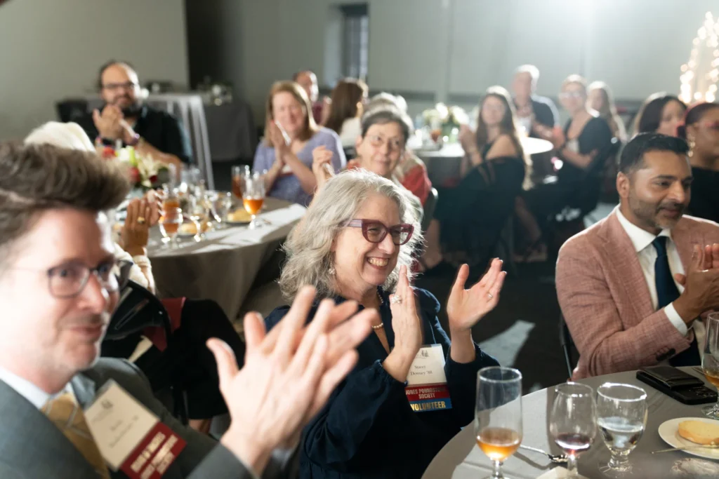 A room view of alumni attendees smiling and clapping.