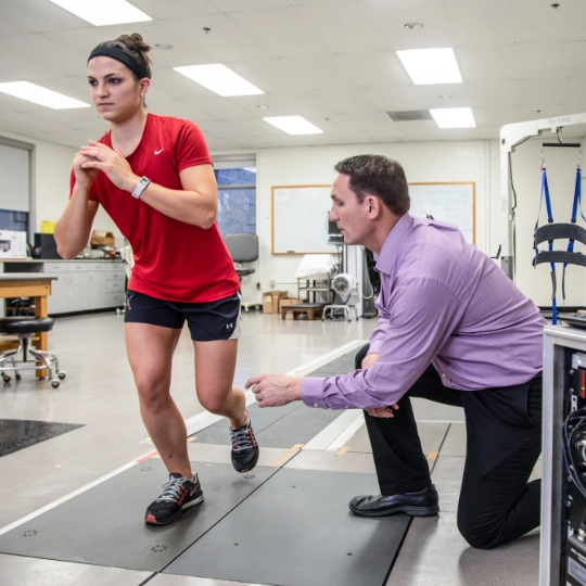 A woman runs in a physical therapy clinical setting with a man monitoring her performance.