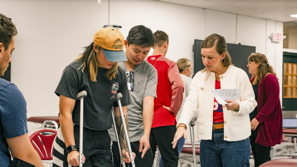 Students work in a physical therapy classroom lab setting and someone is on crutches.