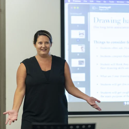 A professor stands with open arms in front of a screen highlighting “Drawing has power” during a class lecture.