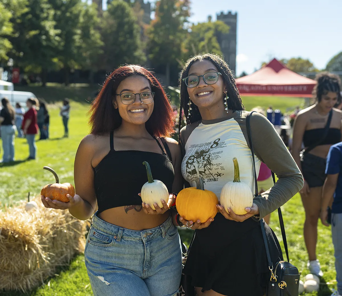 Two people hold pumpkins in the fall sun on the Castle green.