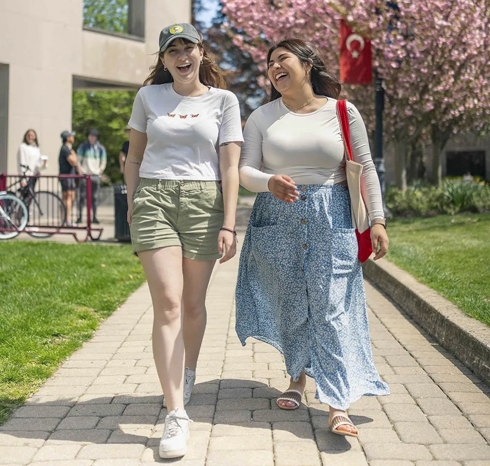 Two Arcadia students laugh as they stroll on a campus walkway.