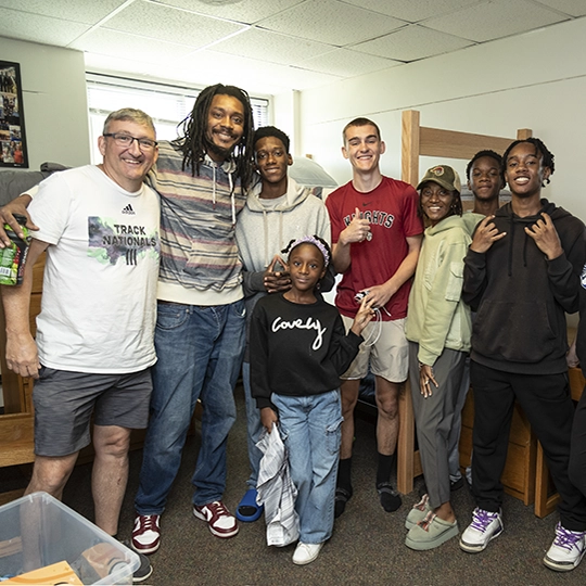 A large family stands together in a dorm room.