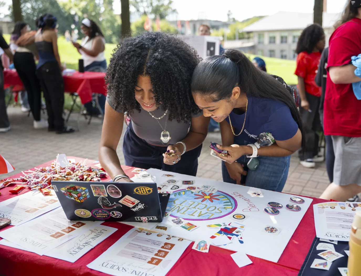 Two people look at a laptop on an event table outside on campus.