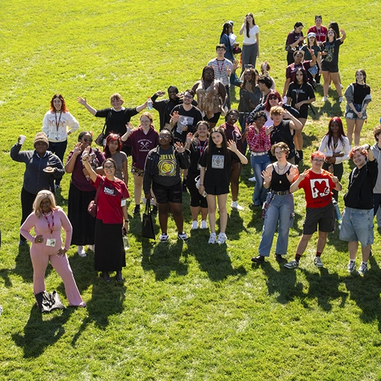 Students stand on the lawn on campus with the sun and shadows.