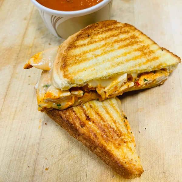 A buffalo chicken grilled cheese sandwich with a red sauce.