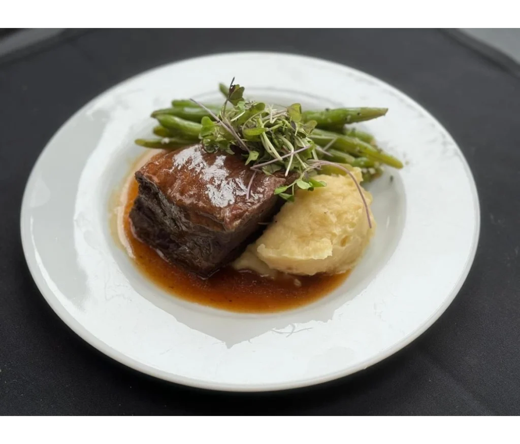 A meat dish served with a biscuit and asparagus on a ceramic white plate.