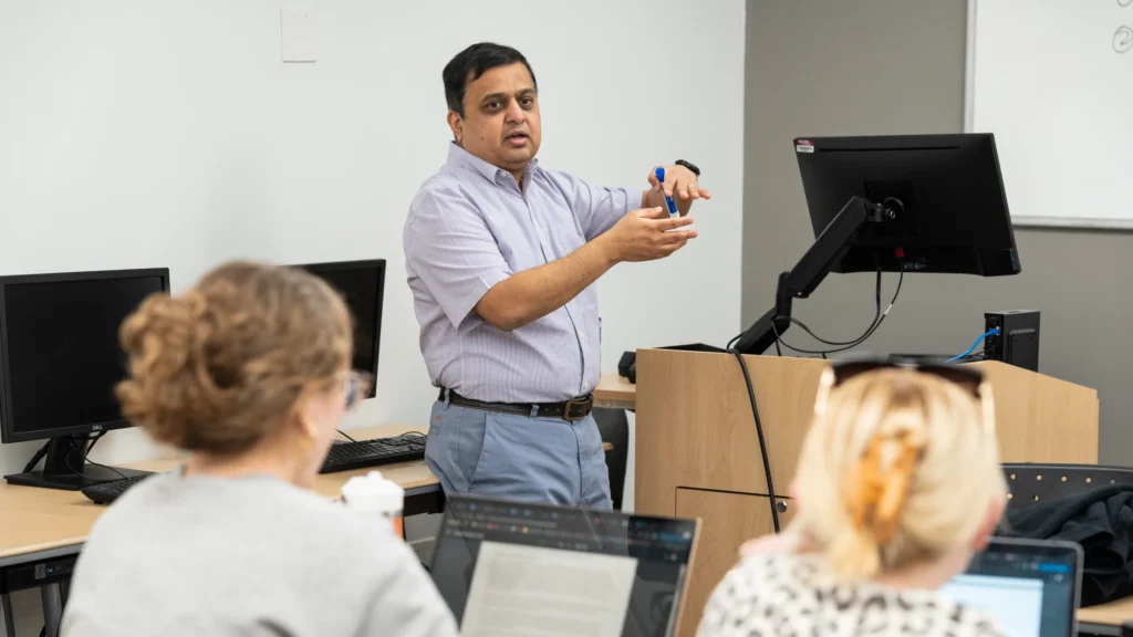 A professor gestures towards a whiteboard while teaching a class.