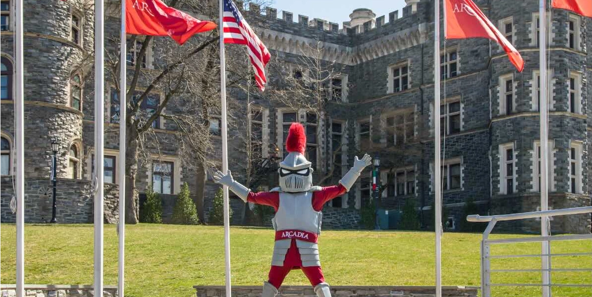Archie the Knight stands with his hands in the air outside of Grey Towers Castle.