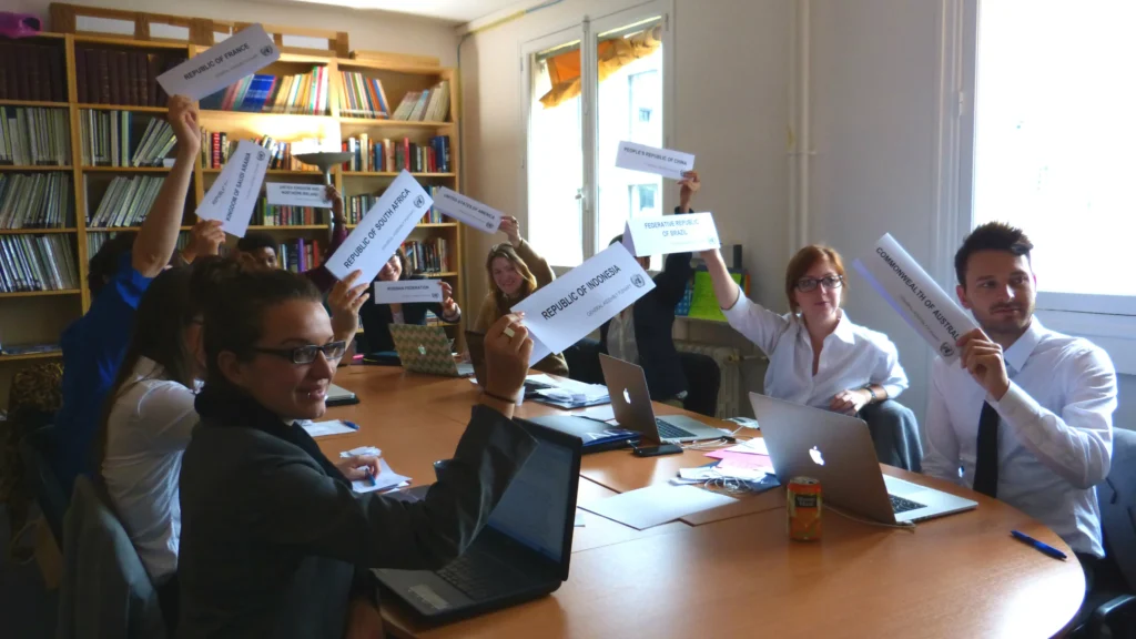 Students seated around a table hold up slips of paper labeled with the names of different nations around the world.