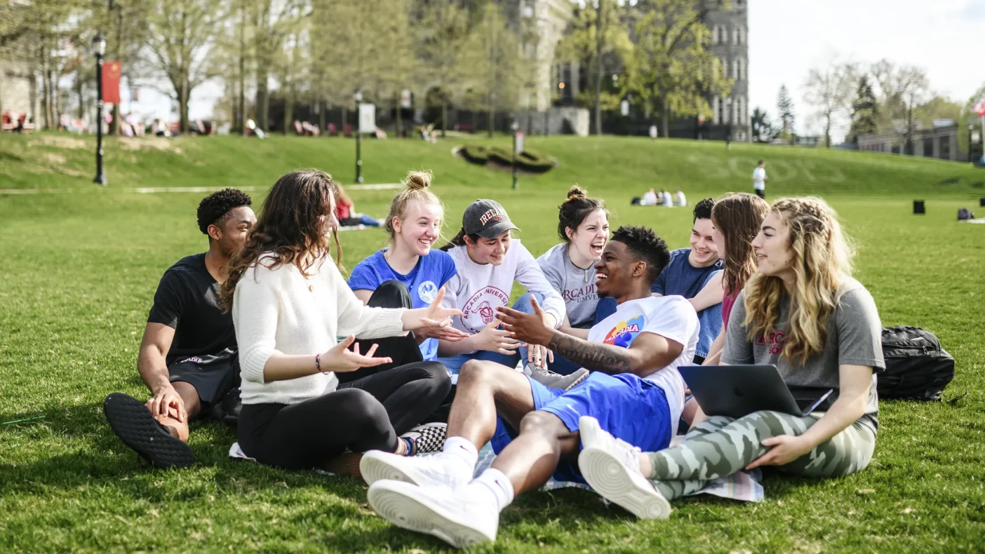 A group of undergraduate students enjoy a chat on the great green by the Castle.