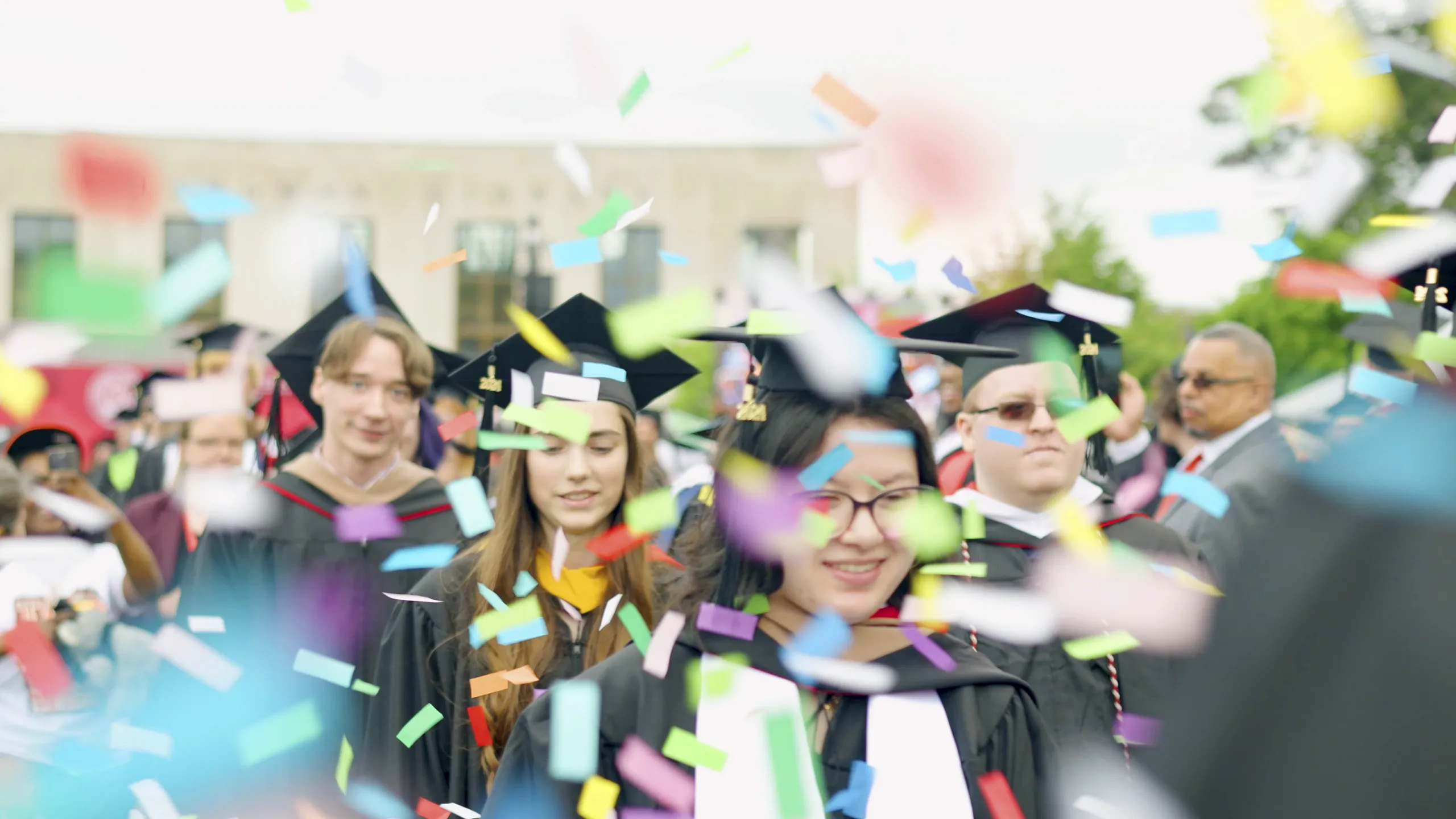 Undergraduate students in a ceremonial march under a sprinkling of confetti during graduation.