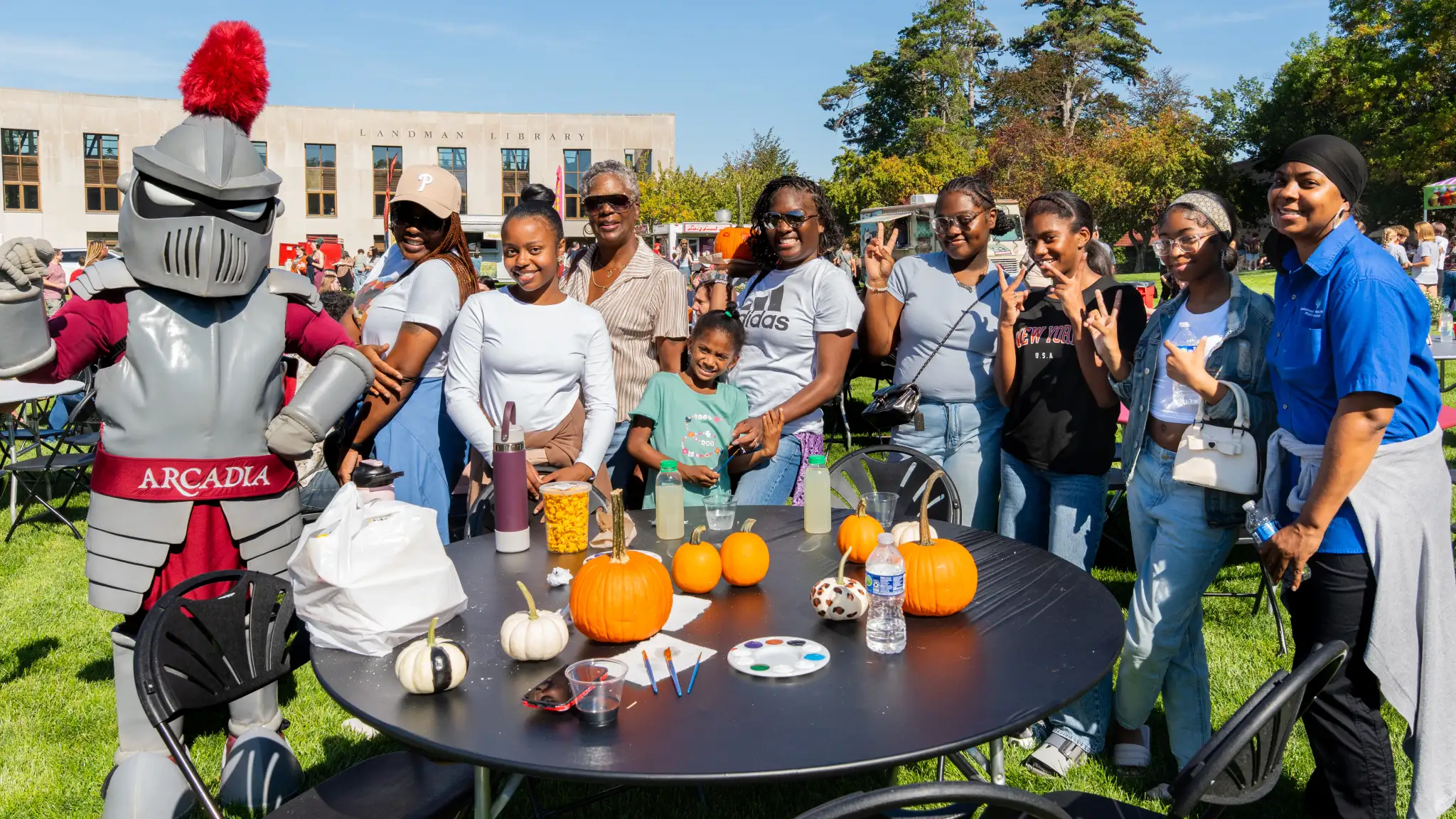 A group of women pose with Archie the Knight at their Arcadiafest table with painted pumpkins on it.