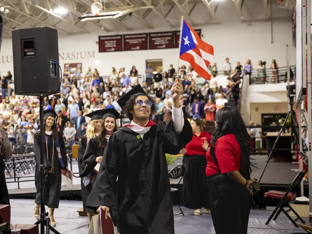 With a flag flying high a student walks through commencement ceremonies.