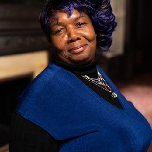 headshot image of woman with tilted head smiling at the camera. She is wearing royal blue and black.