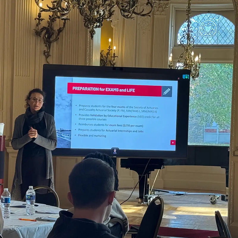 Irina Pogrebivsky, FSA, director of the Arcadia Actuarial Science program, stands at the front of the room and talks with local high school students about the program. Next to Irina is a slideshow with information about the Arcadia program.