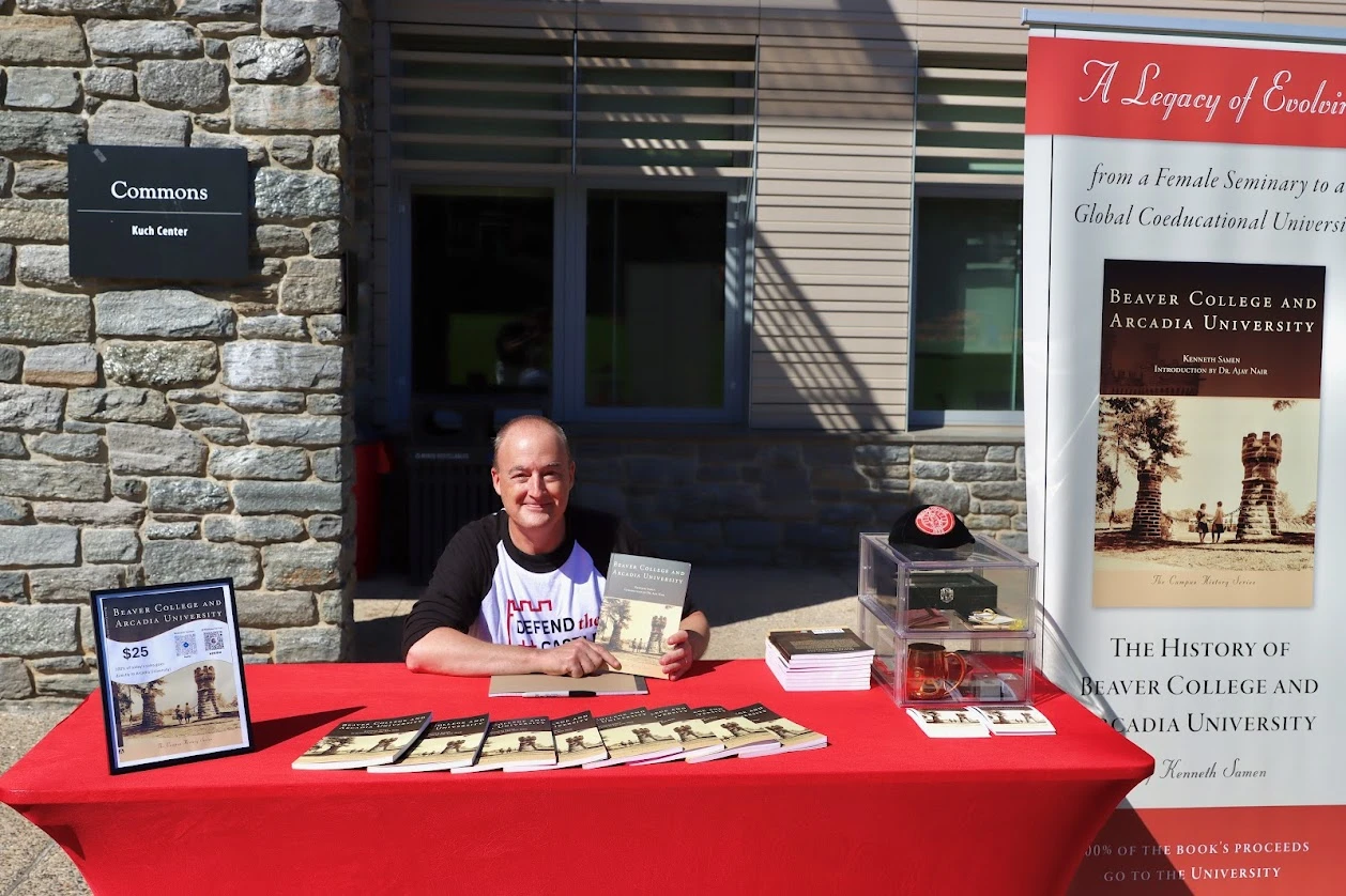 Man sitting at a table smiling, while holding up the book he authored.