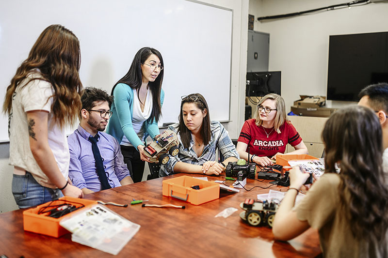 In a classroom setting, six students and a teacher work on model sets.
