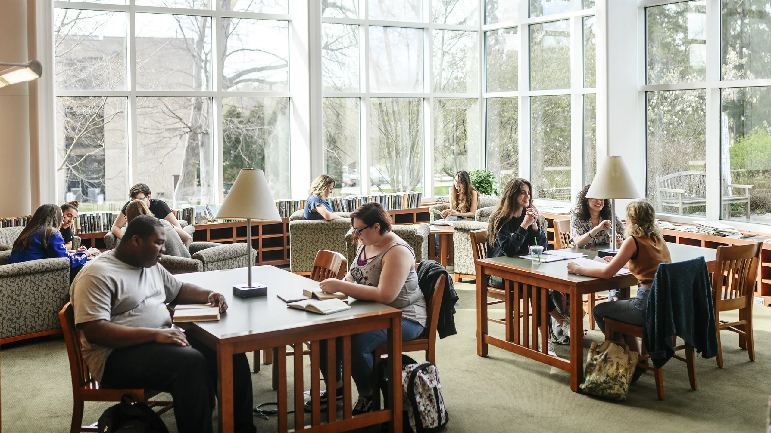 With large sunlit panes of glass as backdrop, student work around tables and comfy chairs in the library.