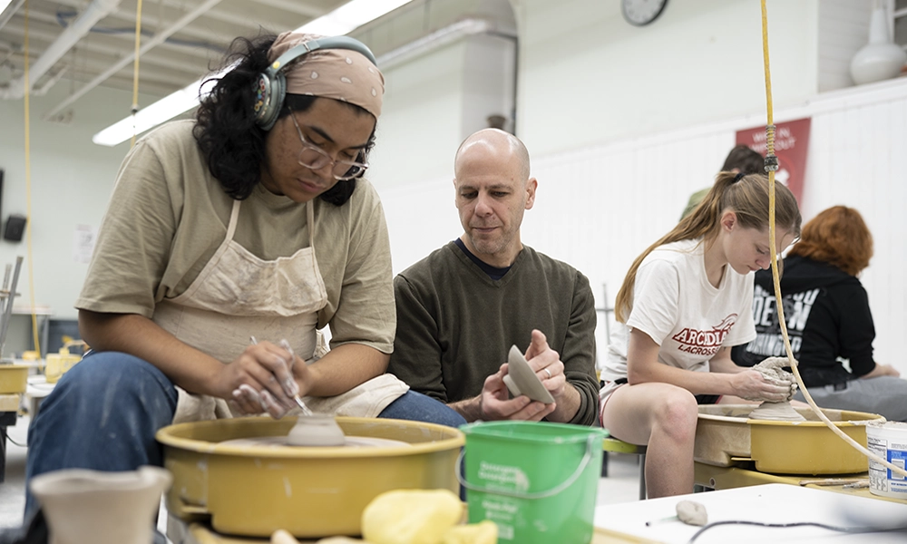 A ceramics wheel is in motion as a student throws a stonewre pot.