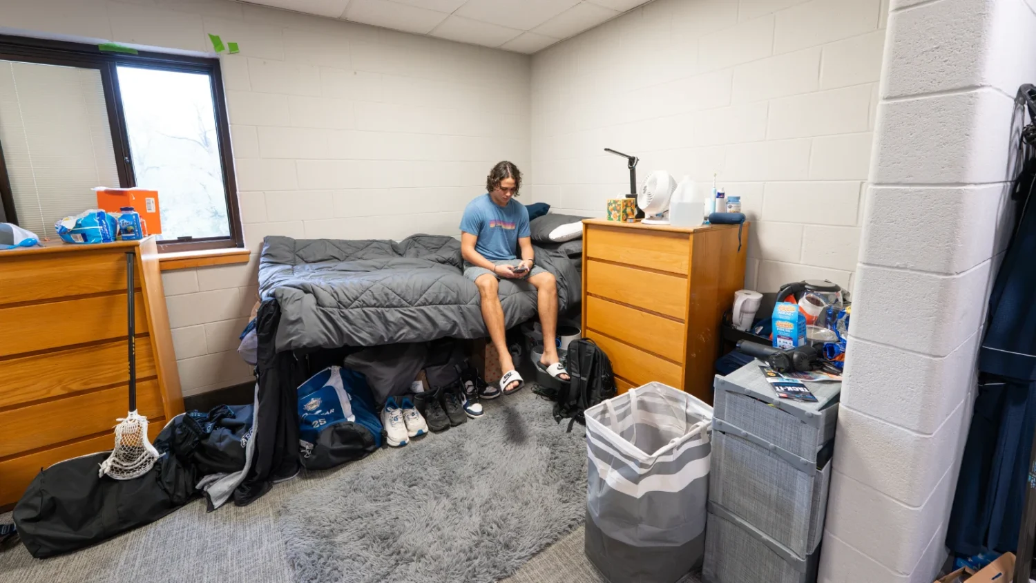 A student sits on his bed on his phone in his bedroom in Knight Hall.