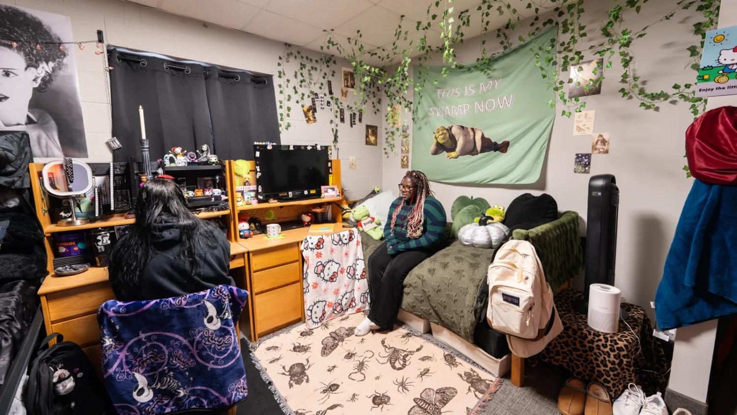 A student sits at her desk on one side of a bedroom while another student sits on her bed on the other side of the room in Knight Hall.