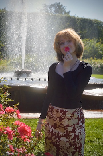 A student wearing a black top and red skirt hold a flower petal to her mouth