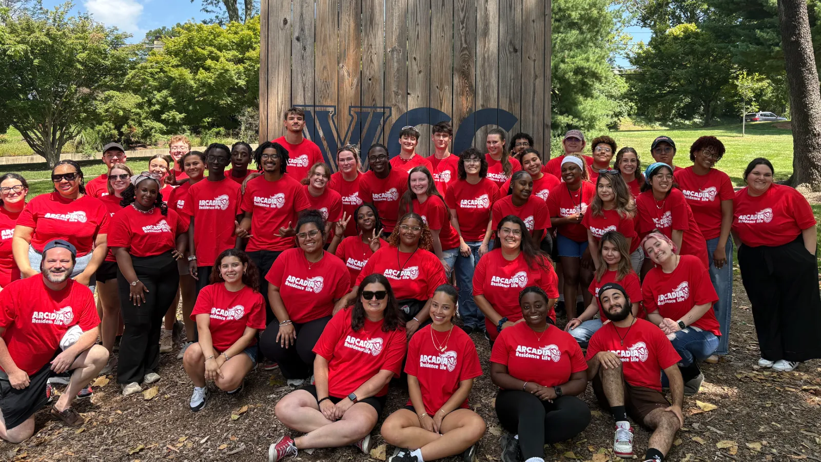 The Arcadia Residence Life team sits outside in their red Residence Life shirts and smile.