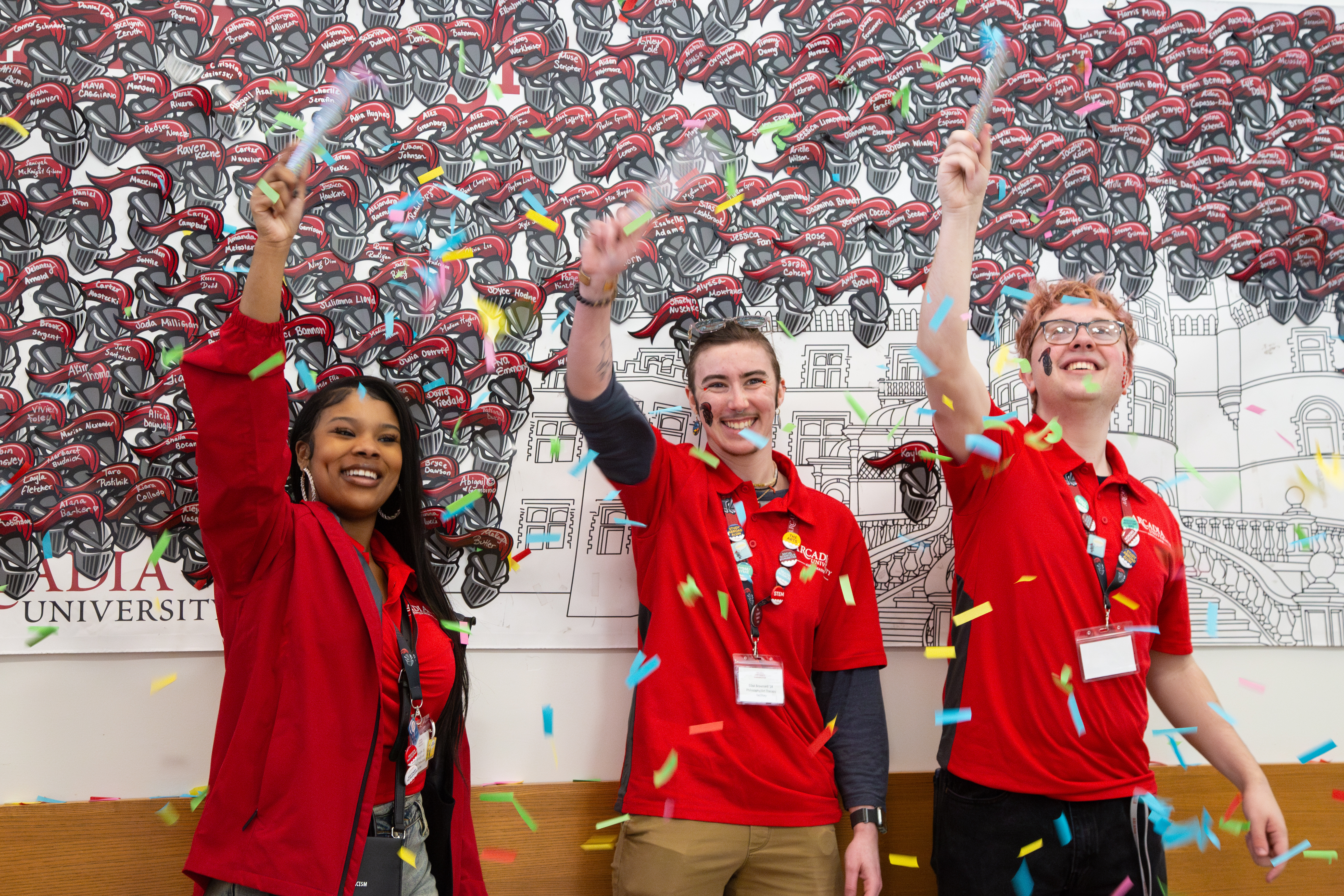 Student Ambassadors throw confetti in front of a wall of new student names