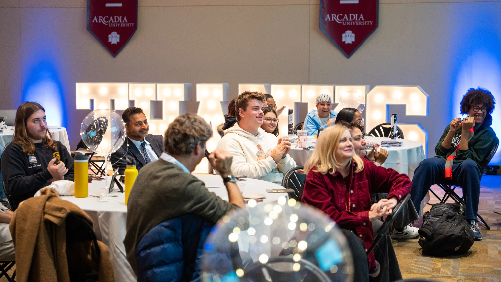 Students, alumni, faculty, and President Nair listen to a presentation at the Thank-a-thon and clap.