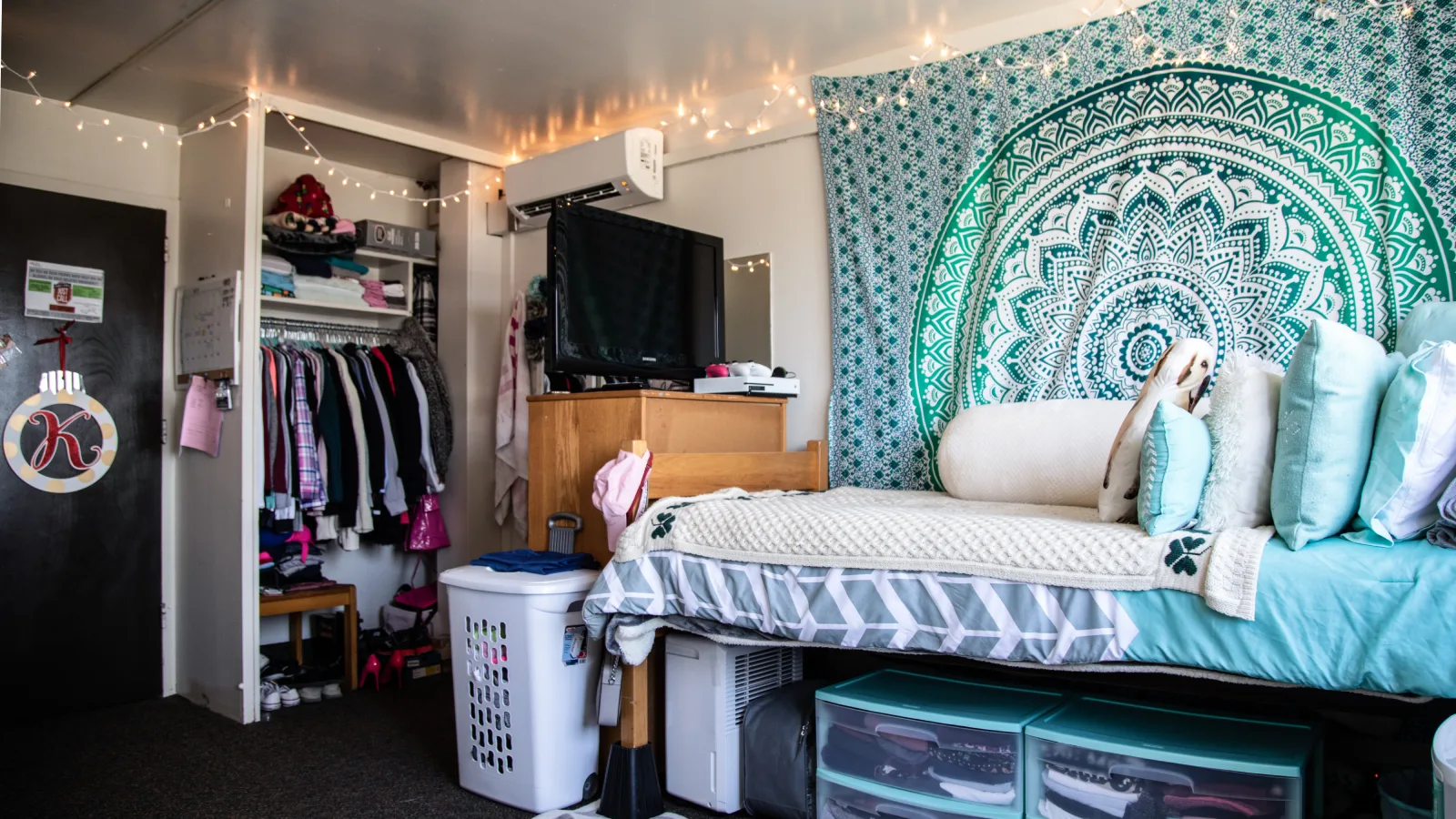 A view inside of a student's dorm bedroom in Thomas Hall, where they have decorated the room with string lights and themed their bed around turquoise/blue and white colors.