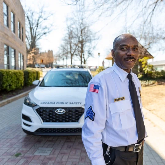 A Public Safety officer poses for a photo in front of a Public Safety vehicle on Arcadia's campus.