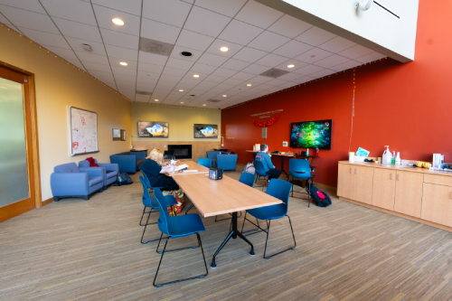 Two students sit in the Commuter Lounge, with one studying at a table and the other playing a game on the TV.