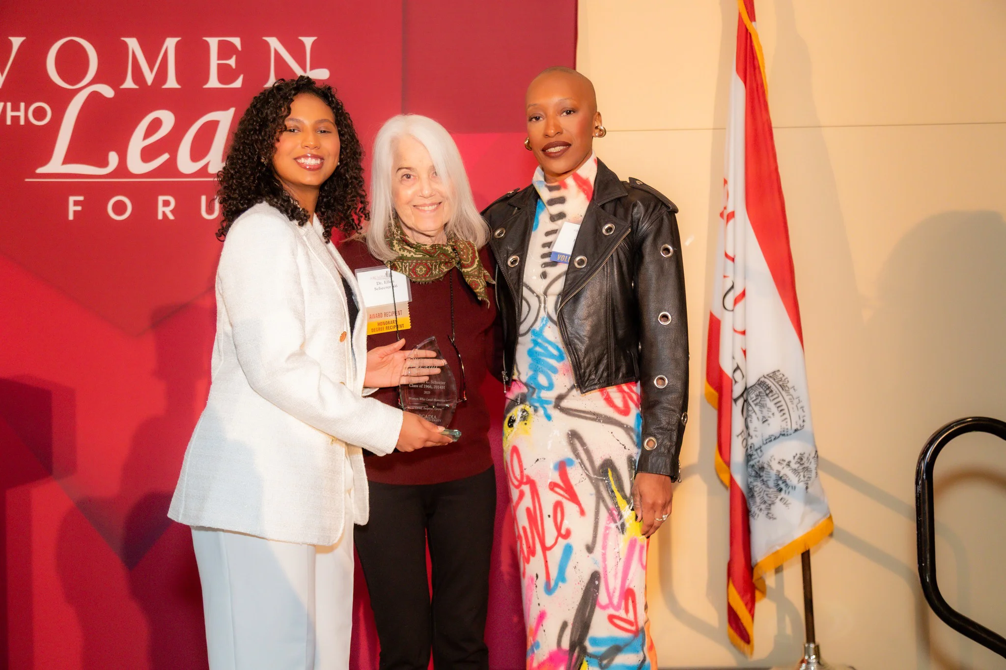 Three women pose for a photo while the woman on the left side holds up a glass award.