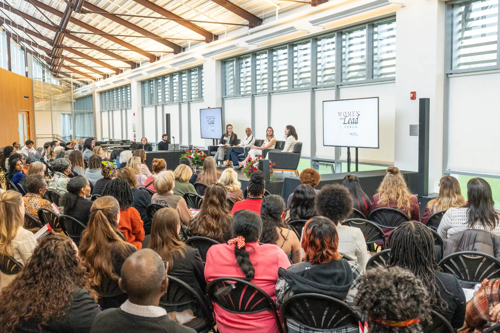 Four women sit in chairs at a panel talking to one another while facing the audience.