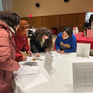 Students, staff, and alumni huddled around a table at the UJIMA gallery event.