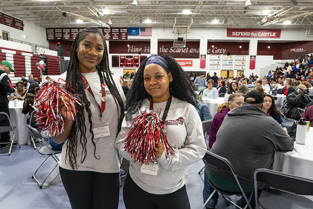 Two students hold scarlet and gray pom-poms during an event in the gym.